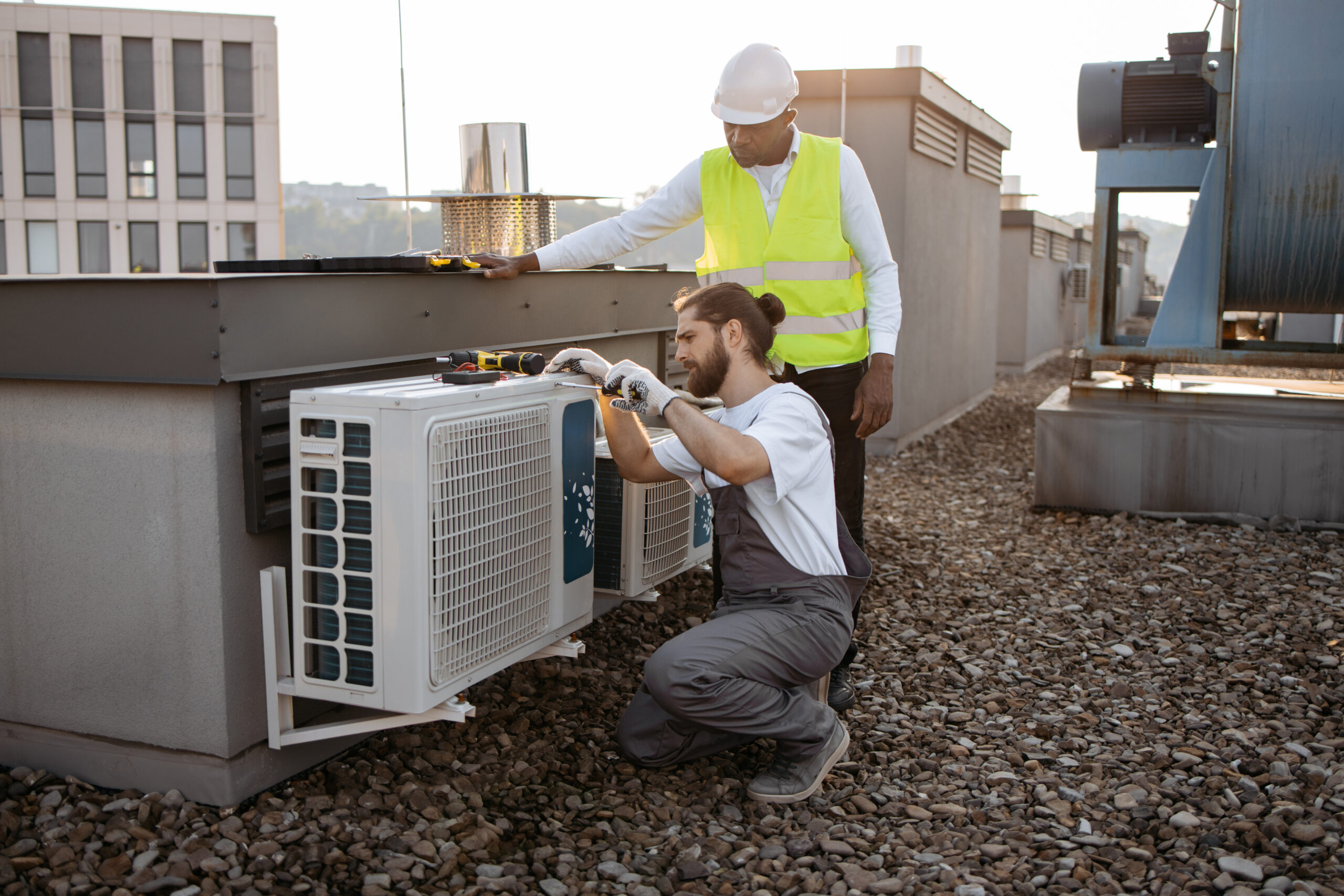 Diverse plant workers repairing air conditioner on rooftop